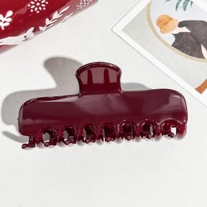 Detailed view of large dark red hair claw clip with glossy finish on textured white background