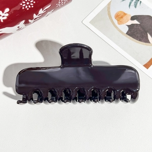 Macro shot of high-gloss dark purple hair claw clip with interlocking teeth on white leather