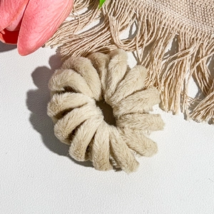 Vue rapprochée d'un chouchou spirale en peluche beige sur cuir blanc avec des tulipes