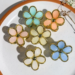 Detailed close-up of six macaron-colored flower hair claws with golden edges on ceramic tray