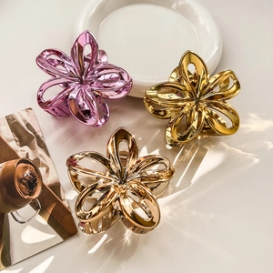 Detailed macro view of three metallic hollow frangipani flower hair claws in gold and purple