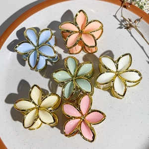 Close-up of six colorful flower hair claws in a ceramic dish with gold metallic borders