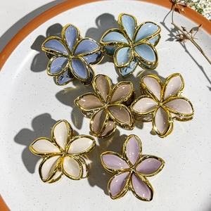 Flat lay of six colorful flower hair claws with gold edges on a ceramic plate