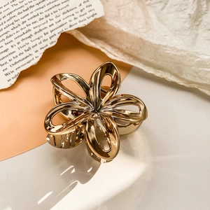 Detail shot of a hollow gold metal frangipani flower claw clip with a polished finish