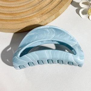 Close-up of a blue marble texture large hair claw clip on a decorative wooden plate