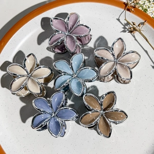 Detailed close-up of six floral hair claws with silver edges in a ceramic dish