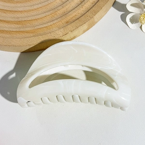 Detail of a white marble texture semi-circle hair claw clip on a rustic wooden tray