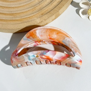 Detail of a large shark hair claw with colorful marble texture on a wooden tray