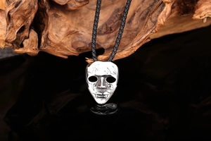Macro shot of silver gothic mask pendant with flame texture on black mirror base