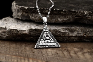 Macro shot of silver Eye of Providence pendant with a braided chain on rock background