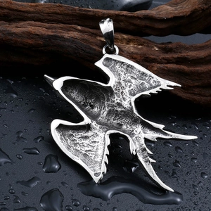 Detailed macro shot of vintage stainless steel swallow bird pendant on wet black surface