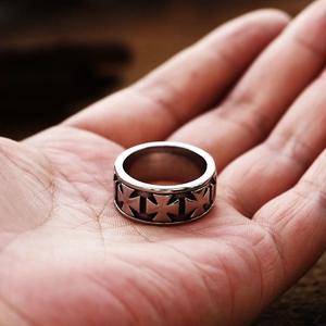 Detailed view of a wide stainless steel cross ring with vintage gothic relief on a hand