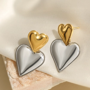 Minimalist gold and silver two-tone stainless steel heart earrings on a satin surface