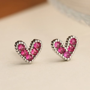 Dettaglio macro di orecchini a cuore con zirconi rosa e bordi con perline in argento