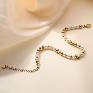Elegante bracciale di perle dorate con pendente a cuore su sfondo di seta calda a forma di S