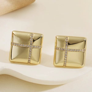 Macro shot of gold square stud earrings featuring cross pattern zircons on white ceramic base