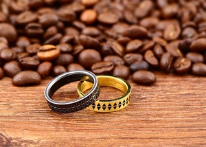 Close-up of black and gold etched rings with geometric patterns on coffee beans background
