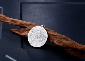 Macro detail of round Viking pendant with textured surface hanging on dark rustic wood branch
