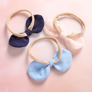 Detailed view of three baby bow headbands in navy, pink, and light blue linen texture