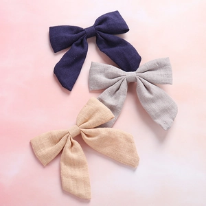 Close-up of three cotton linen bow hair clips in purple, grey, and apricot colors