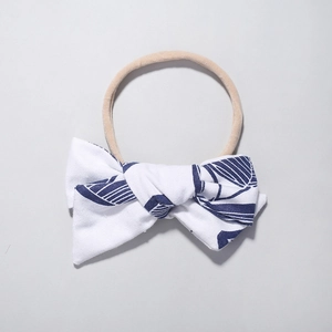 Dettaglio fascia in nylon per neonati con fiocco bianco e motivi di foglie tropicali blu