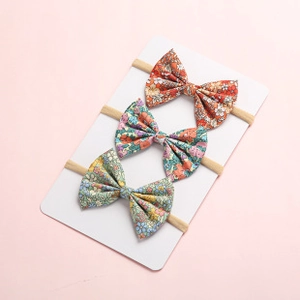 Detailed set of three floral print baby bow headbands in warm autumn colors on display card