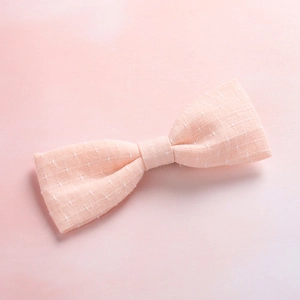 Close-up of a soft pink fabric bow hair clip with white textured cross-stitch patterns