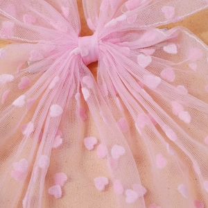 Gros plan du nœud papillon en résille rose avec motifs de cœurs et texture dentelle