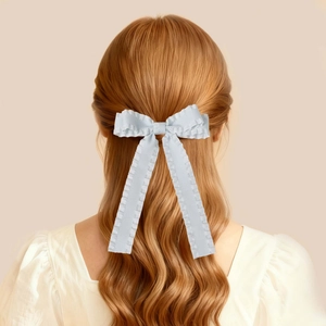 Dettaglio di un fermaglio per capelli con fiocco in raso bianco, bordi ondulati e nastri