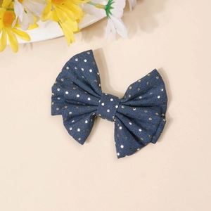 Detail of denim blue bow hair clip with gold sequins and heart pattern on beige background
