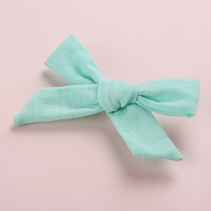 Close-up of mint green cotton bow hair clip with textured fabric on a pink background