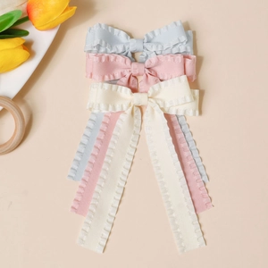 Dettaglio di tre fermagli per capelli in raso nei colori azzurro, rosa e bianco crema