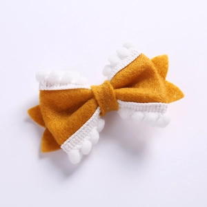 Détail d'un nœud à cheveux en feutre jaune avec bordure en dentelle à pompons blancs