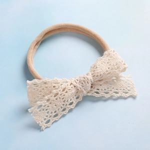 Dettaglio del fiocco in pizzo color crema sulla fascia elastica per neonati in nylon morbido
