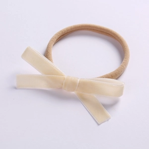 Close-up of stretchy nylon baby headband with a soft beige velvet bow on white background