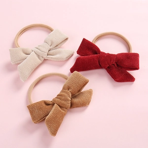 Three-pack of corduroy bow baby headbands in off-white, burgundy and brown on pink background