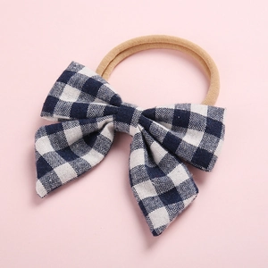 Détail d'un nœud à carreaux bleu foncé sur bandeau bébé beige en nylon souple