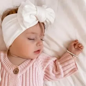 Close-up of baby wearing a soft white nylon headband with large bow during peaceful sleep