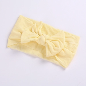 Detail of soft cream nylon baby headband featuring a handcrafted knit bow on white background