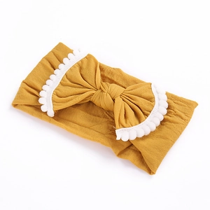 Close-up of ginger yellow baby headband with knit texture and white pom-poms detail