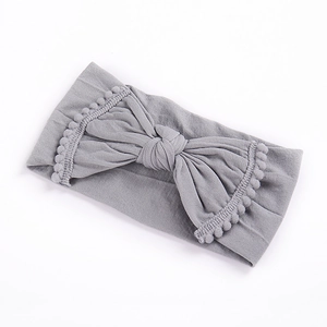 Detail of grey elastic baby headband featuring a large bow and pom-pom tassel edges
