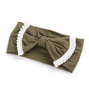 Detail of olive green baby headband featuring a large bow with white pom-poms lace trim