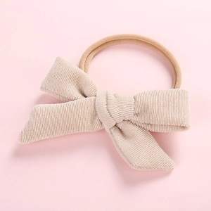 Detail view of cream corduroy bow hairband with elastic nude pink band on pink surface
