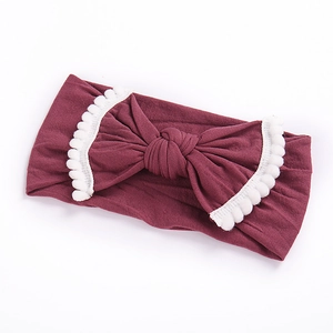 Elastic burgundy baby headband with large bow and white pom-pom trim detail