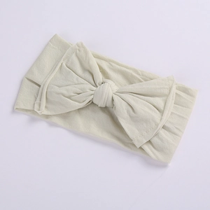Detail of soft cream knitted baby headband featuring a large bow on white background