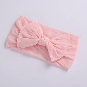 Close-up detail of soft pink baby headband featuring a large bow and seamless fabric texture