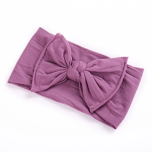 Elastic baby headband in purple soft knit fabric with a large bow detail on white backdrop
