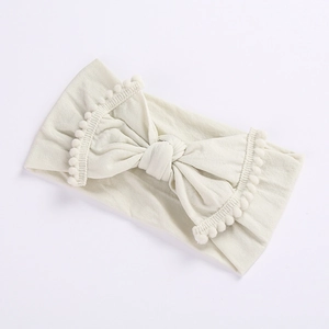 Detail of baby headband with oversized bow and pompom fringe on soft cream fabric