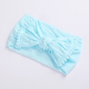 Detail of light blue baby headband featuring a soft bow and decorative pom-pom trim