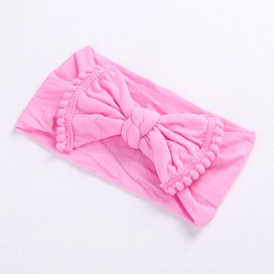 Detailed view of baby headband featuring large pink bow with pom-pom trim texture
